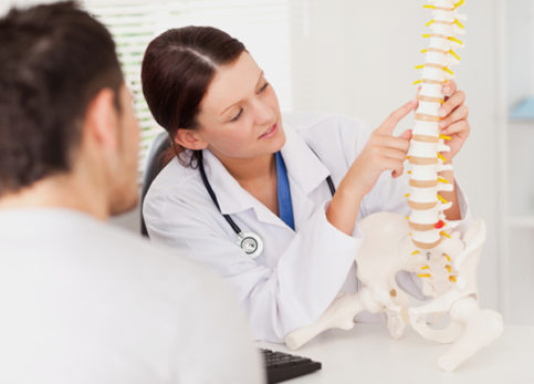 Female practitioner pointing to something on spine model for male patient